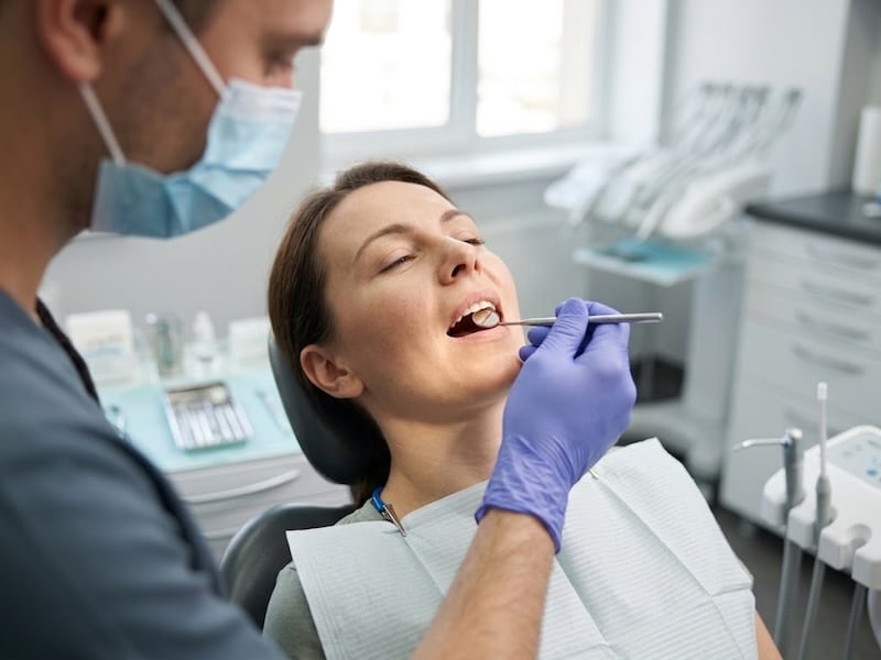 دندانپزشک در حال بررسی لثه بیمار با آینه دندانپزشکی در کلینیک